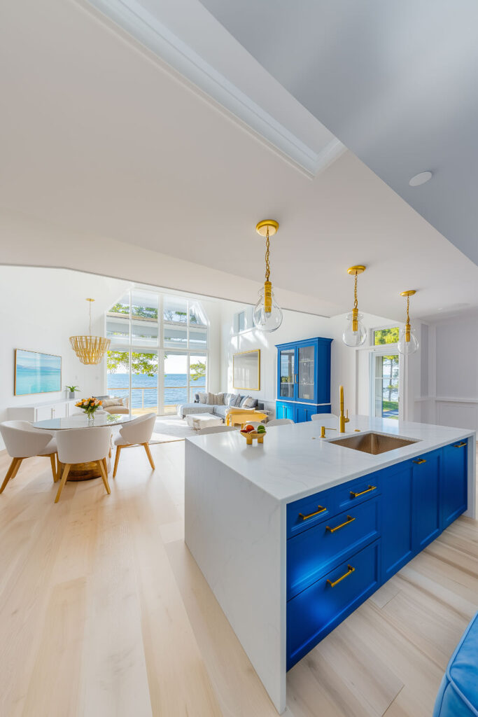 A vibrant coastal kitchen design with bold blue cabinetry, gold accents, and a spacious island that seamlessly blends into the airy interior.