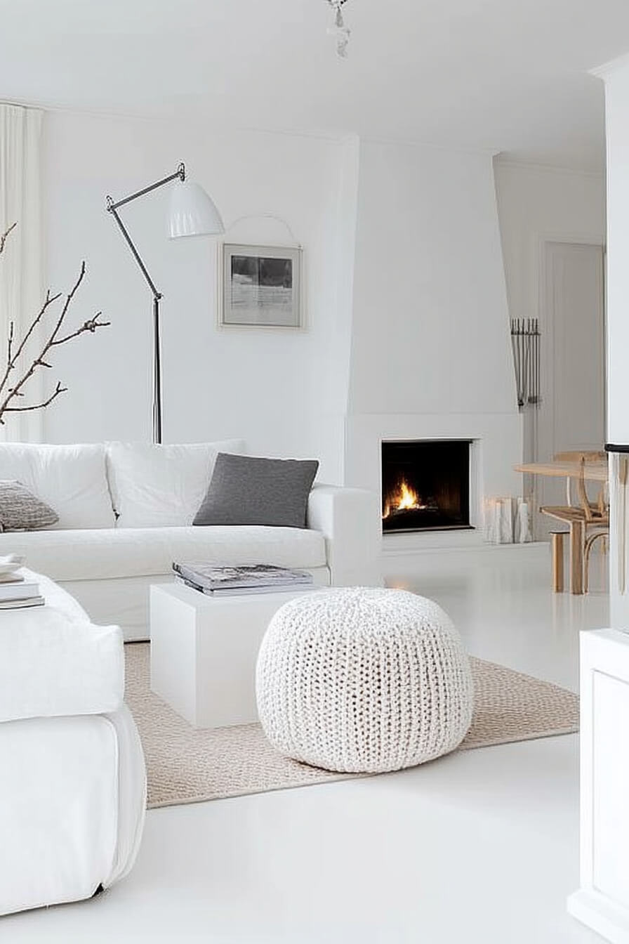 A cozy white living room with a fireplace, soft couches, and a big window letting in natural light.