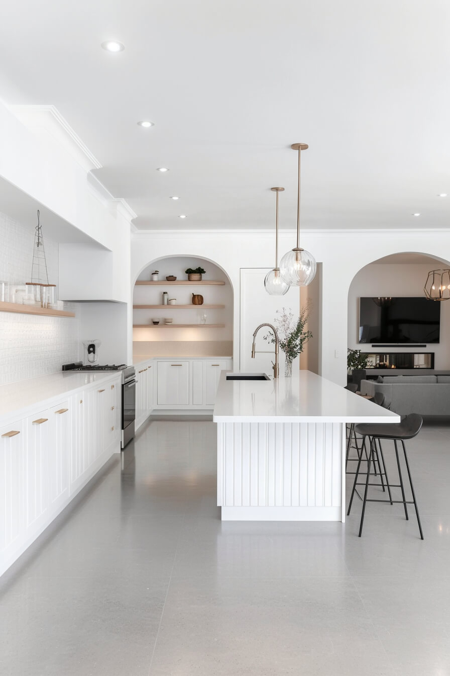 A modern white kitchen with a spacious island, minimalist shelving, and elegant pendant lighting, showcasing a clean Kitchen Design White and a contemporary Kitchen Room Design.